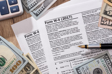 w4 tax form with money, pen and calculator on desk.