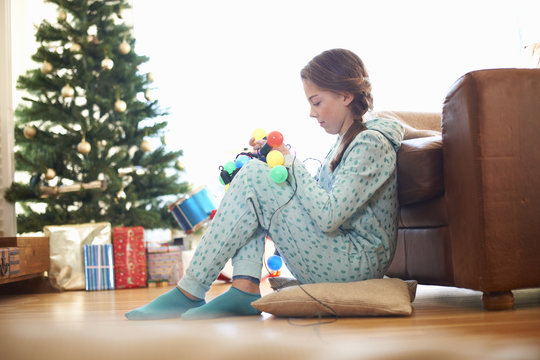 Girl sitting on living room floor untangling christmas lights at christmas