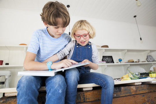 Girl grabbing storybook from brother on kitchen counter