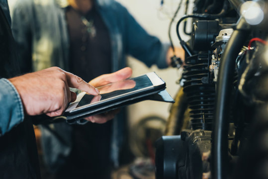 Two mature men, working in garage, using digital tablet, close-up