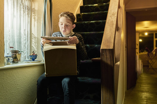 Boy sitting on stairs blowing dust from photograph frame