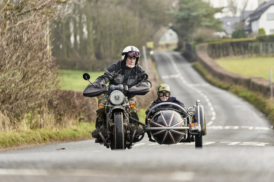 Senior man and grandson riding motorcycle and sidecar on rural road