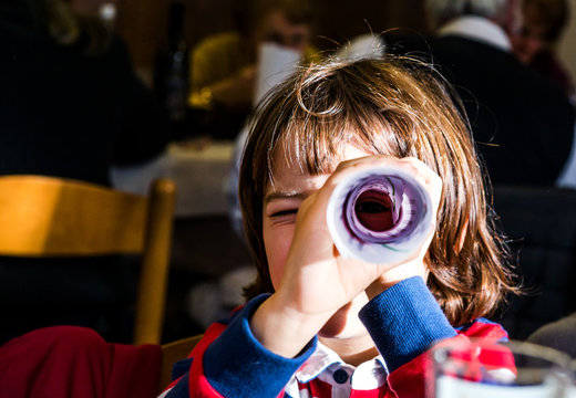 Portrait of boy looking through rolled paper in cafe