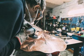 Metalworker polishing copper in forge workshop