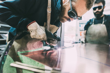 Metalworker cutting copper sheet with welding torch in forge workshop
