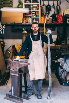 Portrait of metalworker leaning on anvil in forge workshop