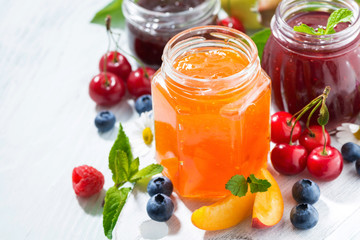 assortment of sweet jams and seasonal fruits on white background, top view closeup