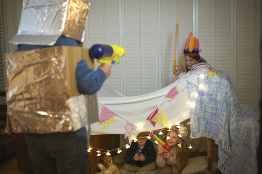 Senior man in robot costume having dress up play fight with grandchildren