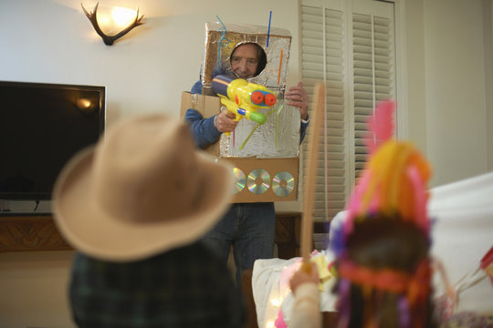 Senior man in robot costume shooting toy guns with dressed up grandchildren