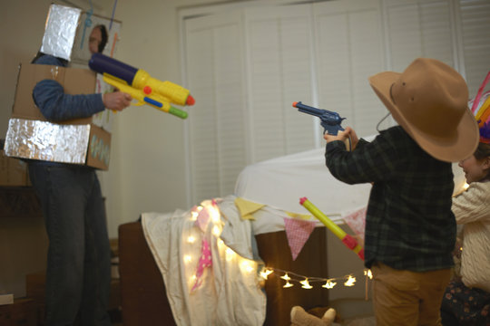 Senior man in robot costume shooting toy guns with dressed up grandchildren