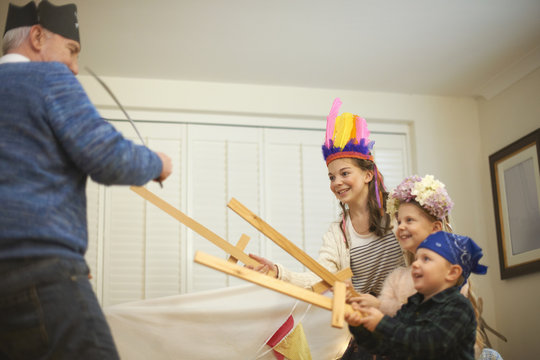 Senior man in pirate hat having sword fight with dressed up grandchildren