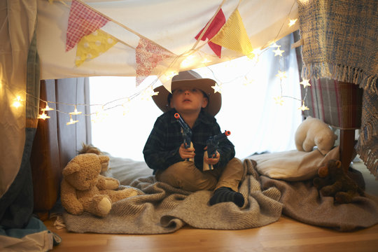 Portrait of cute boy in cowboy hat holding toy guns in bedroom den