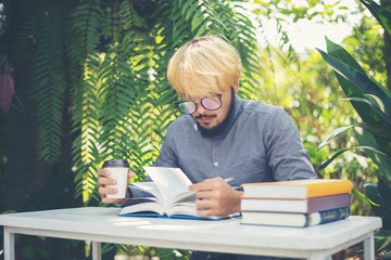 Young handsome beard man reading book in backyard. Learning or Education concept.
