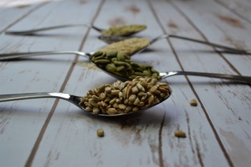 Seeds in spoons on white wood background