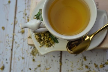 Herbal tea with dried herbs and gold spoon on white wood background