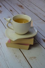 Cup of tea on top of paperback books on white wood background