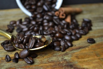 Coffee beans spilling out of white cup with cinnamon sticks and gold spoon 