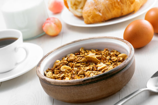 Granola, croissant, milk and fruits on a table. Healthy breakfast with coffee. International vegetarian meal.
