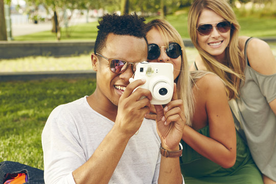 Young man and friends photographing with instant camera in park