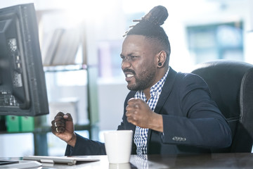 African American office worker with collected rasta hair exulting happy reading good news on his...