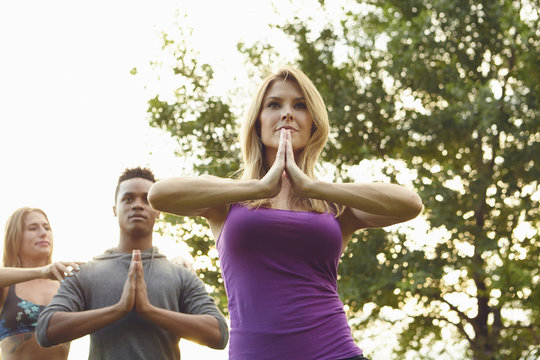Male and female adults practicing yoga with hands together in park
