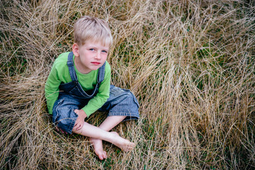 Naklejka na ściany i meble Little boy in blue jeans and green shirt sitting on the grass. Childhood vacations concept