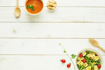 Light summer meal concept. Green salad with pasta, cherry tomato, quail eggs. Cold tomato soup (gazpacho) with croutons on a white table. Copy space. 