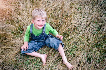 Naklejka na ściany i meble Little boy in blue jeans and green shirt sitting on the grass. Childhood vacations concept