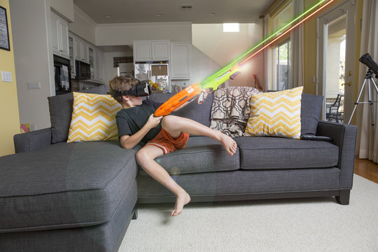 Young boy on sofa, wearing virtual reality headset, firing laser guns, digital composite