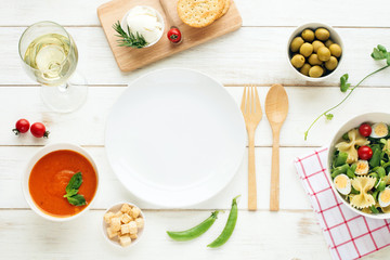 Light summer dinner / supper concept. Green salad with pasta, cherry tomato, quail eggs, olive oil. Cold tomato soup (gazpacho), croutons, green olives and glass of cold white wine. 