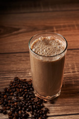 Coffee and banana smoothie in a glass on a wooden background