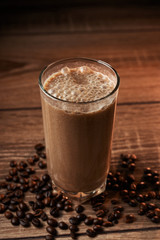 Coffee and banana smoothie in a glass on a wooden background