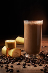 Coffee and banana smoothie in a glass on a wooden background