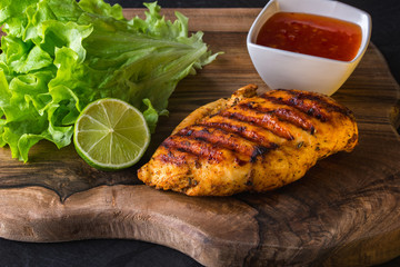 Grilled chicken breast served with green fresh salad, lime and chili sause on wooden cutting board