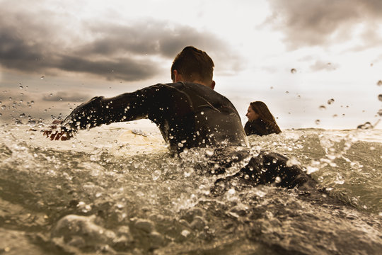 Two friends in sea, paddling on surfboards, rear view