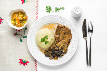 Cooked pork chop steak with mushrooms and mashed potatoes on white table