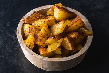 Grilled potatoes in wooden bowl on black background