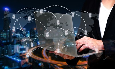 smart businessman in suit using his laptop or computer notebook, business and technology concept with world map social media network connection on blurred night city background, color tone effect.
