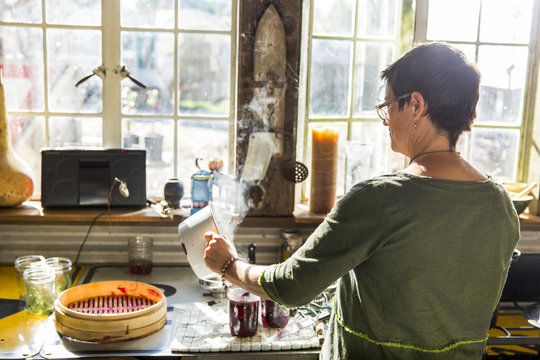 Rear view of woman pouring beetroot into preserves jars in kitchen