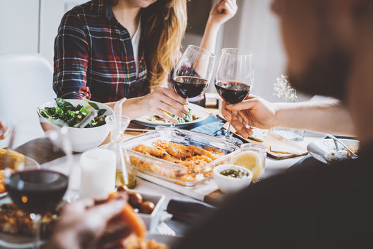 Happy friends cheering with glasses of red wine at restaurant with healthy food, group of people enjoying and toasting at home, togetherness and friendship concept, filtered image