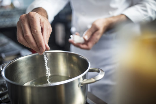 Chef putting salt in pan of water on stove, close-up