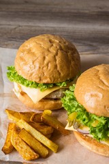 Home made hamburger with chicken, onion, cucumber, lettuce and cheese on wooden table with potato fries