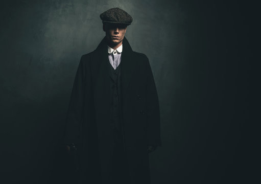 Mysterious retro 1920s english gangster with flat cap and black coat.