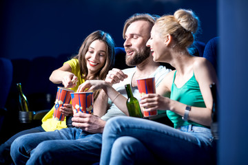 Happy friends watching film sitting together with popcorn in the cinema