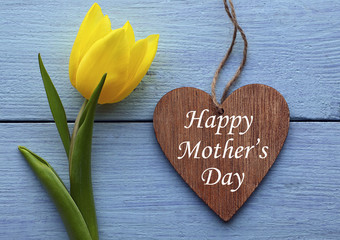 Happy Mother's Day.Yellow tulip and decorative wooden heart on blue wooden background.Mother's Day greeting card.Selective focus.