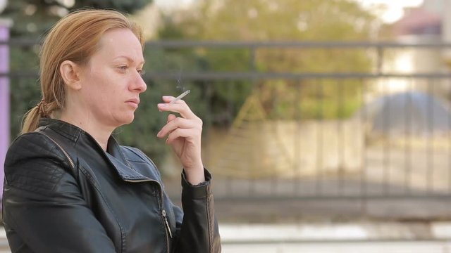 Sad woman without makeup nervously smokes in the street