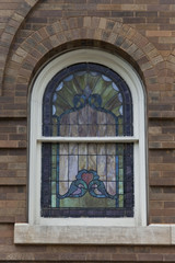 Arched stain glass window on brick wall.