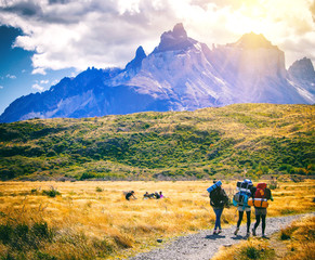 Group of travelers with backpacks walk along a trail towards a mountain ridge.Backpackers and...