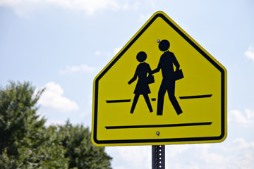 Pedestrian crossing sign surrounded by cloudy blue sky and green tree tops.