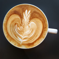 Top view of a mug of latte art coffee on black background.